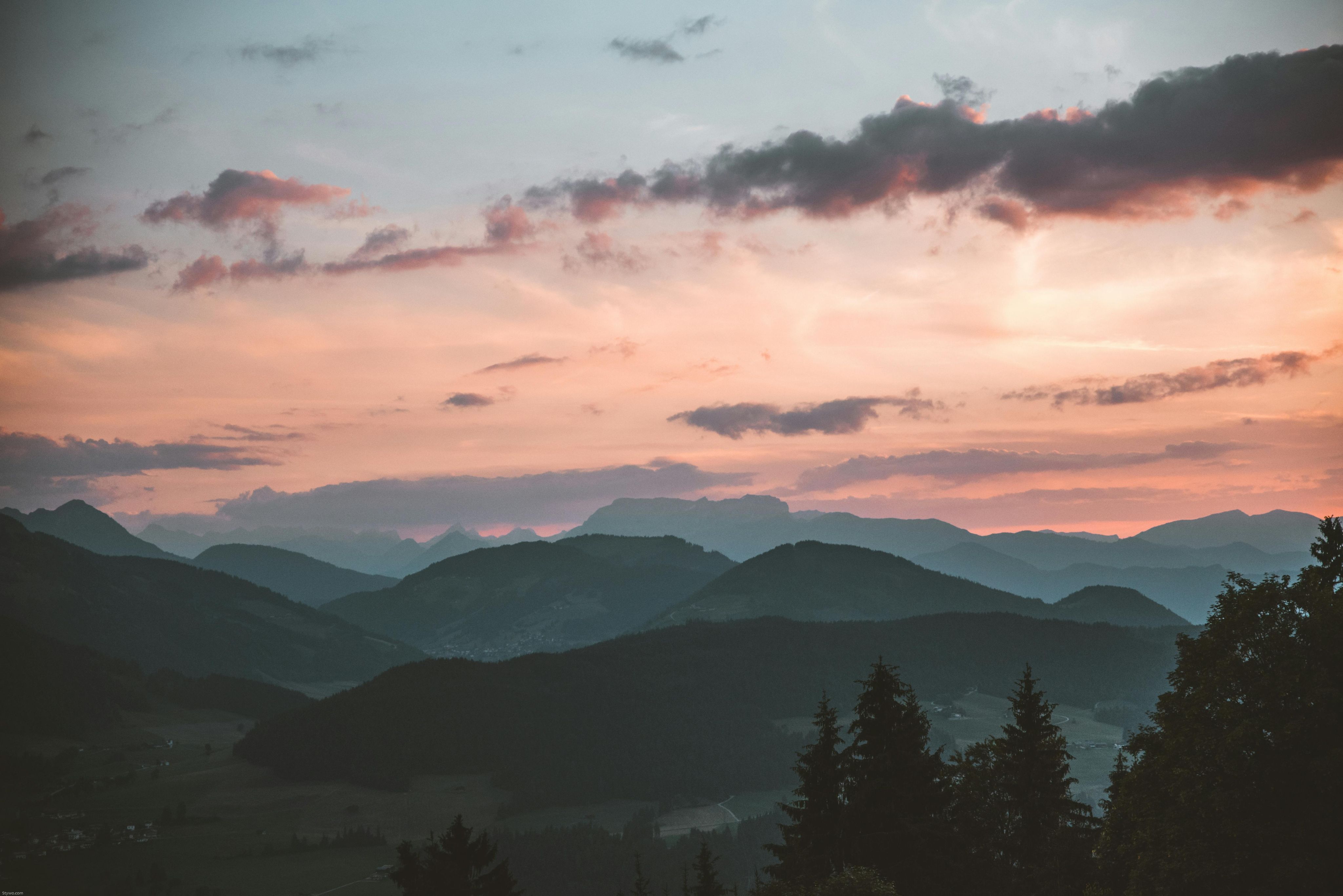 mountain silhouettes at sunset with dramatic clouds and a soft pastel sky in the background